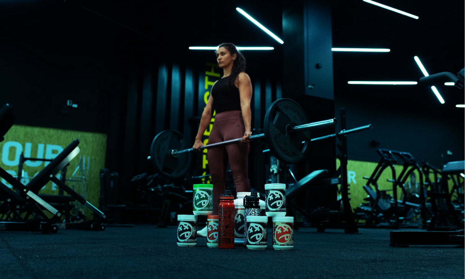 Female athlete lifting weights in a gym with SKELETON Nutrition supplements displayed in front
