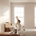 Skeleton Nutrition Magnesium Glycinate supplement bottle on a bedside table next to a woman stretching in bed.