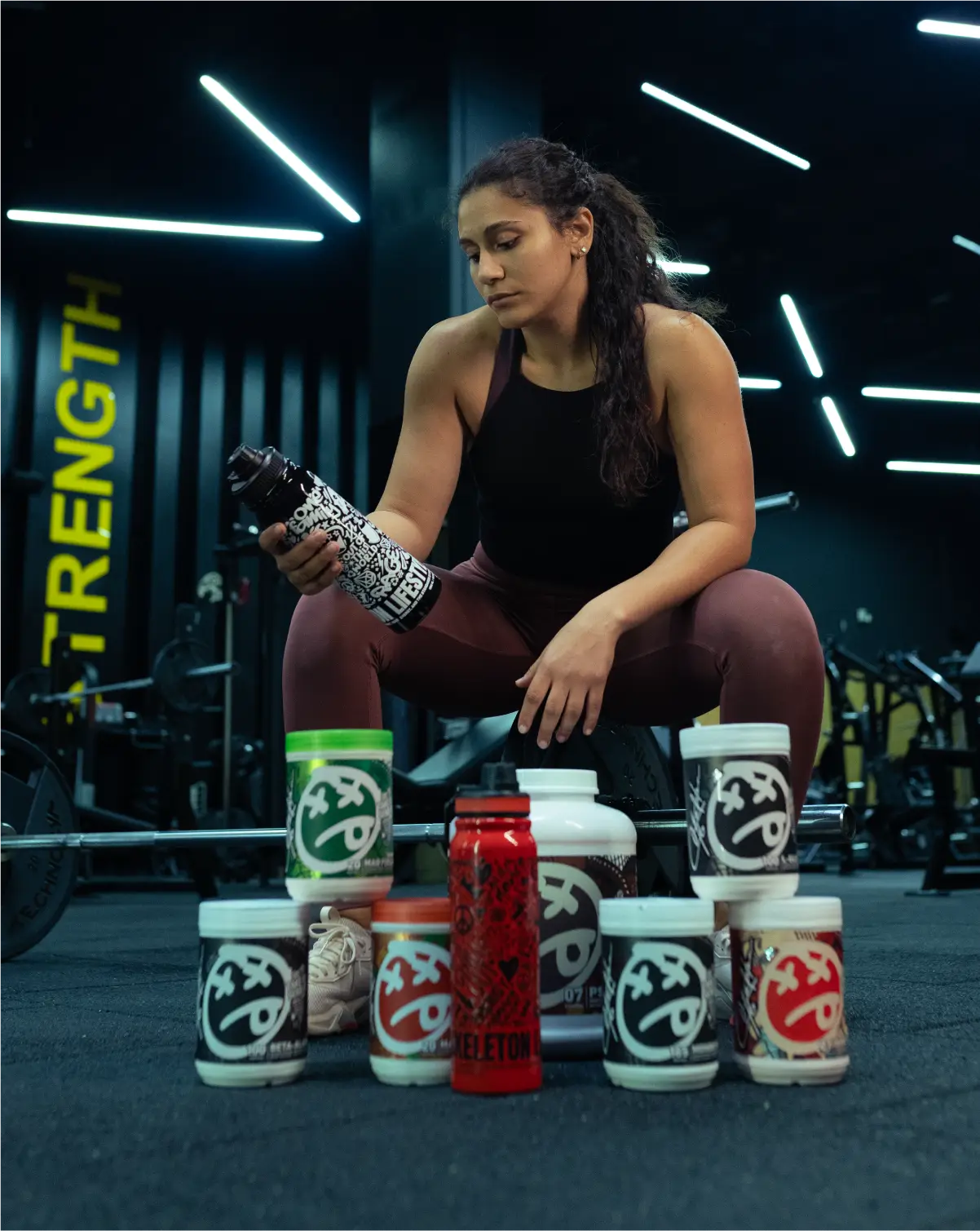 Female athlete with SKELETON® supplements and shaker bottle inside gym during workout session