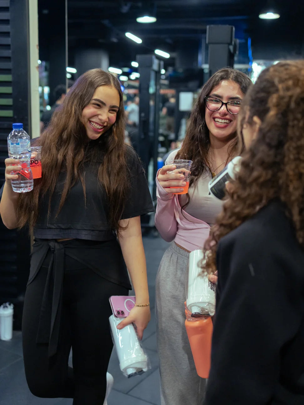 Two women standing together, one holding a skeleton shaker and the other a spooky drink, in an indoor setting.